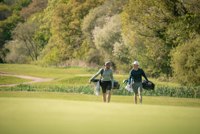 Two golfers walking with bags across fairway