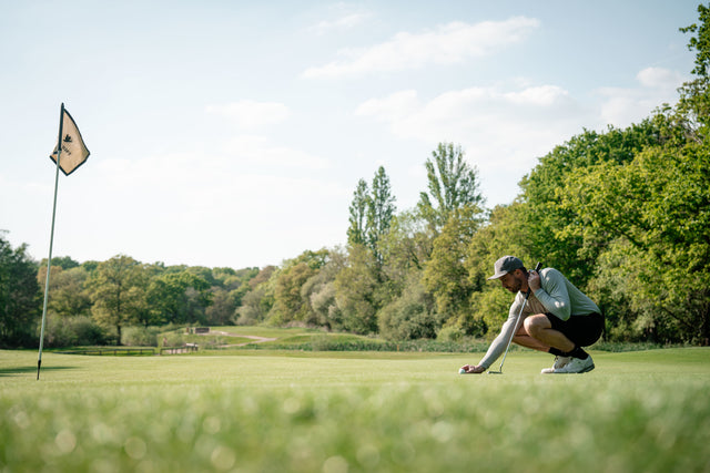 Golfer lining up a putt on a green under clear skies