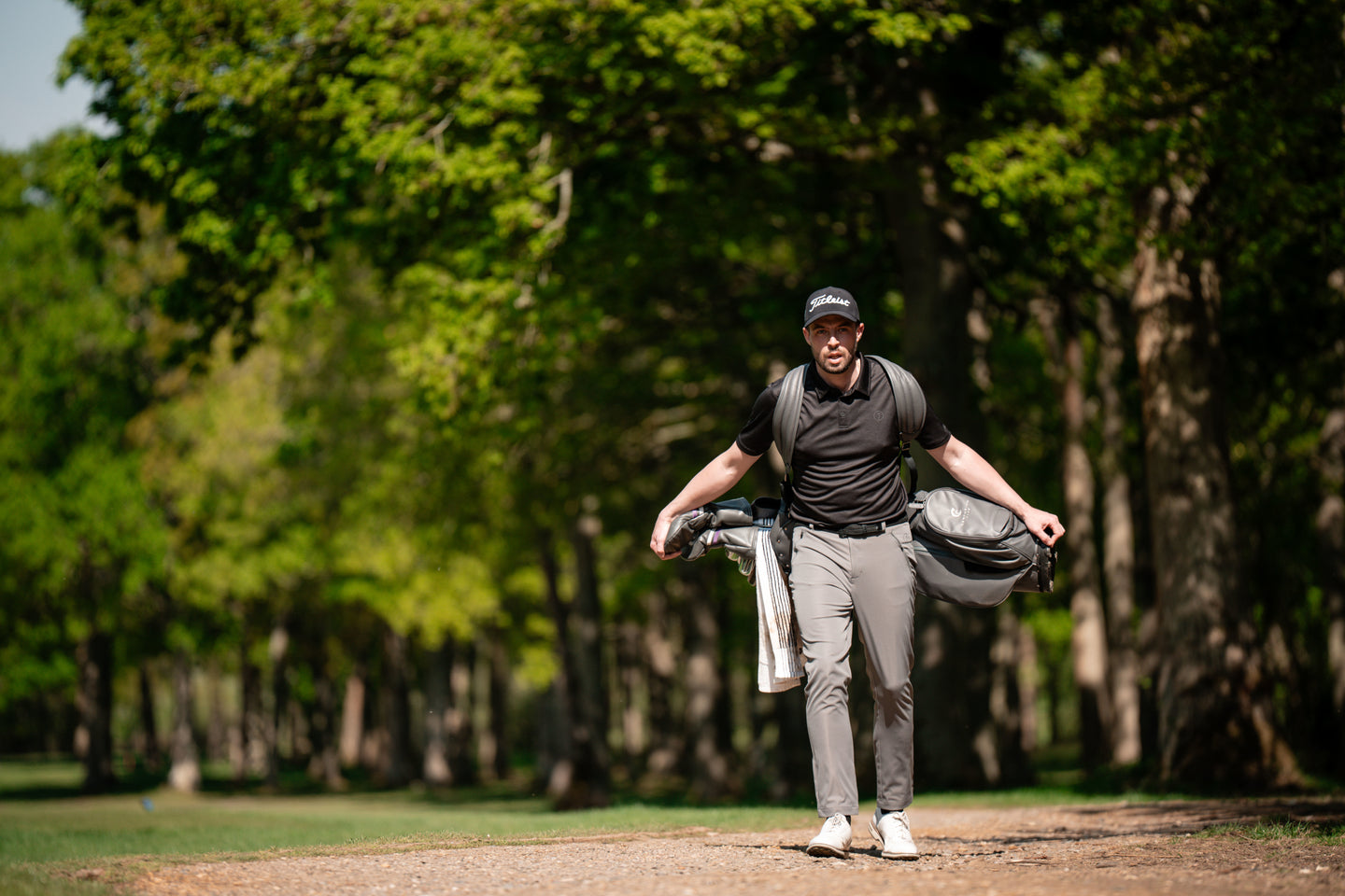 Golfer carrying clubs in woodland path