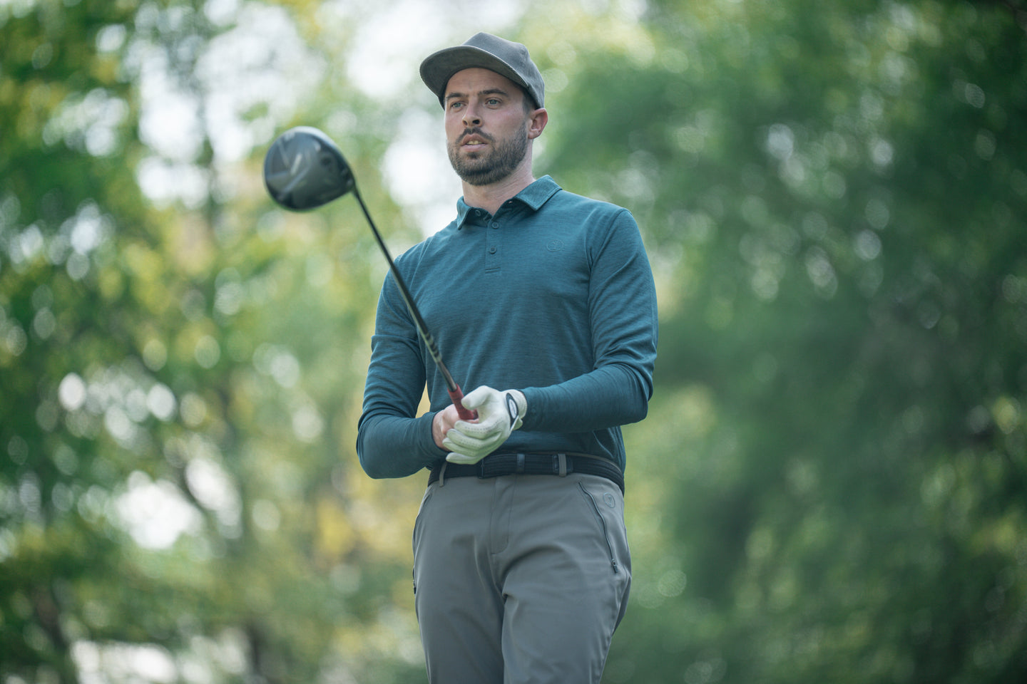 Golfer holding driver in teal golf polo