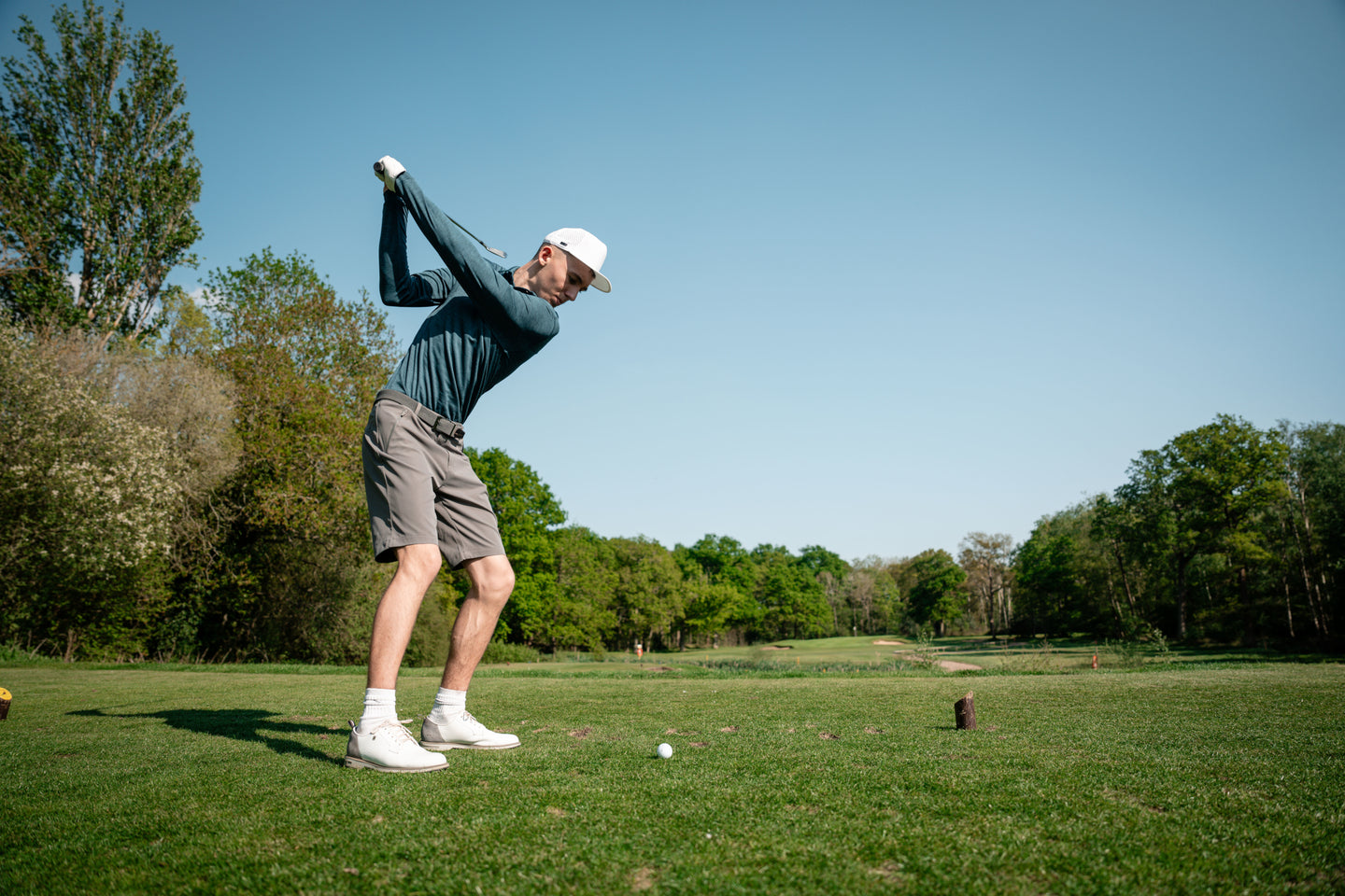 Golfer in shorts teeing off under clear sky